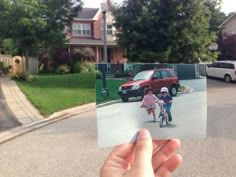 a person holding up a polaroid with a child on a bike in the street