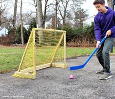 a young boy hitting a ball with a plastic stick in front of a yellow goal