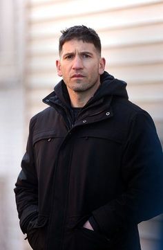 a man standing in front of a building wearing a black jacket and looking at the camera