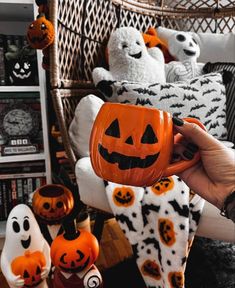 someone is holding a pumpkin mug in front of some stuffed ghost's and other halloween decorations