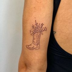 a woman with a tattoo on her arm holding a boot and flowers in the vase