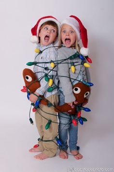 two children wearing christmas lights and santa hats standing next to each other with their mouths open