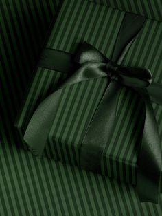 a green gift box with a black bow on it's side and striped wrapping paper