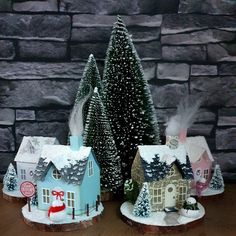 two small houses are decorated with fake trees and snow on the top, while another one is standing in front of a stone wall