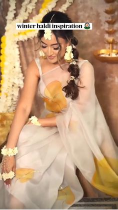 a woman in a white and yellow sari with flowers on her head sitting down