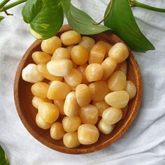 a wooden bowl filled with yellow beans next to green leaves on a white tablecloth