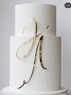 a white and gold wedding cake with the letter k on top