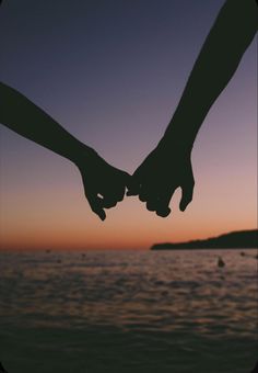 two people holding hands while standing in front of the ocean