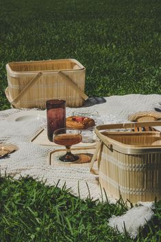 two wicker baskets sitting on top of a blanket next to wine glasses and food