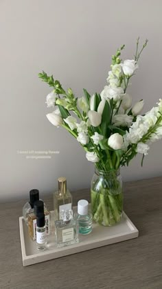 a vase filled with white flowers sitting on top of a table next to perfume bottles