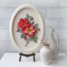 a white vase sitting on top of a table next to a plate with flowers painted on it