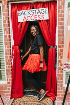 a woman standing in the doorway of a brick building with red curtains and a sign that says backstage access