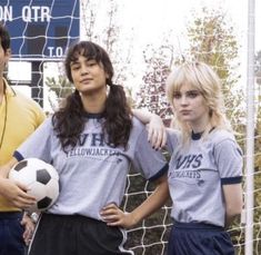 three people standing next to each other with a soccer ball in front of a net