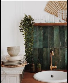 a white sink sitting under a green tiled wall next to a counter with plates and cups on it