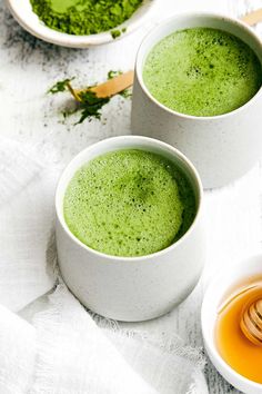 two white bowls filled with green tea next to some honey dips on a table