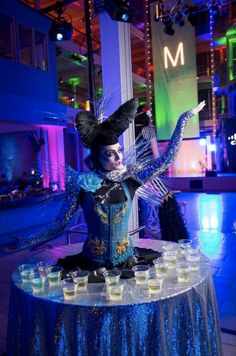 a table topped with cups filled with drinks and a doll dressed as an evil queen