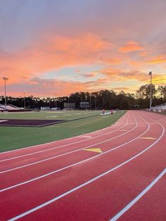 the sun is setting over a track with red and green running tracks in front of it