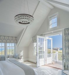 a bedroom with white walls and windows overlooking the ocean is pictured in this image, there are two chandeliers hanging from the ceiling