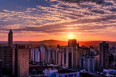 the sun is setting over a city with high rise buildings in the foreground and mountains in the background