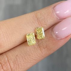 a woman's hand holding two yellow diamond earrings