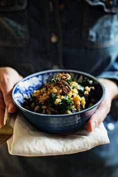 a person holding a blue bowl filled with corn and broccoli on top of a napkin