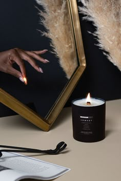 a candle sitting on top of a table next to a mirror and a person's hand