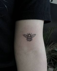 a small black and white bee tattoo on the left inner arm, with an insect in it's center