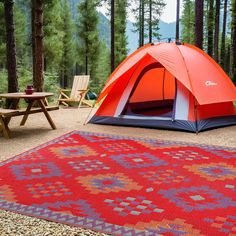 a tent is set up in the middle of a forest with picnic tables and chairs around it