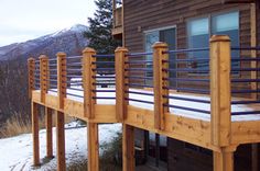 a wooden deck with metal railings and snow on the ground in front of a cabin