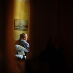 an older man sitting in a chair looking out the window at something on the wall