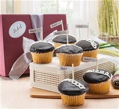 cupcakes with black frosting and football decorations on a wooden tray in front of a gift box