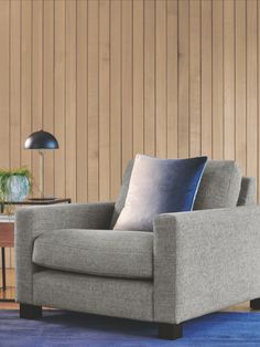 a gray chair with blue pillows on it in front of a wood paneled wall