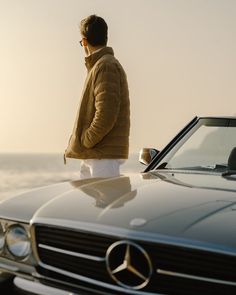 a man standing on top of a car talking on a cell phone next to the ocean