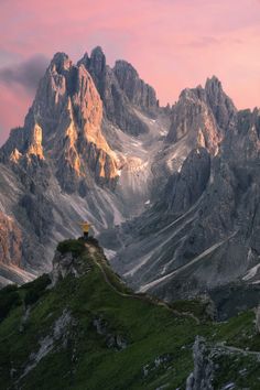 there is a small house on the top of a hill with mountains in the background