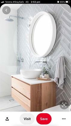 a bathroom with a round mirror above the sink and a wooden cabinet below it in front of a white tiled wall