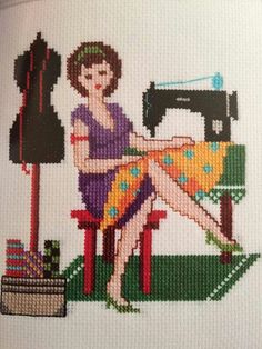 a woman is sitting on a chair with a sewing machine in front of her cross stitch pattern