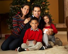 a family sitting on the floor in front of a christmas tree holding a tablet computer