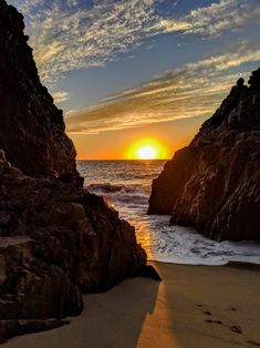 the sun is setting behind some rocks on the beach