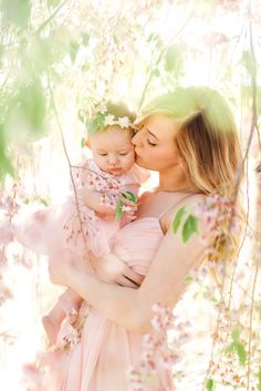 a woman holding a baby in her arms and kissing it's face with the sun shining