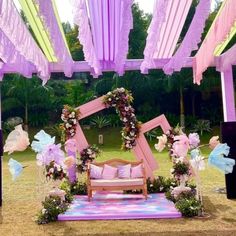 a wooden bench sitting under a canopy covered in purple and pink flowers on top of a grass field