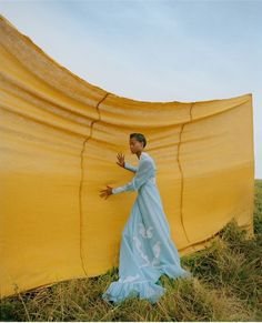 a woman in a blue dress standing next to a yellow tarp