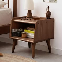 a nightstand with books, camera and glasses on it next to a bed in a bedroom