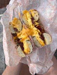 a person holding a hot dog with cheese and other toppings in their hands,