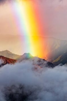 a rainbow shines brightly in the sky above clouds and mountains on a cloudy day