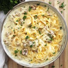 a pan filled with pasta and mushrooms on top of a wooden cutting board next to parsley