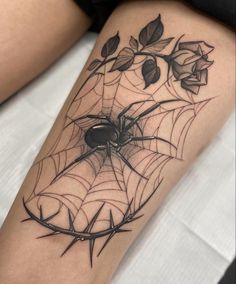 a spider web tattoo on the leg with flowers and leaves in it's center