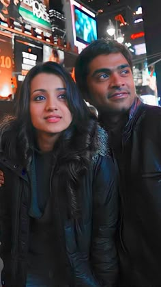 two people standing next to each other in front of a building with neon signs on it