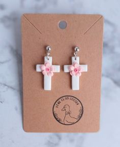 a pair of white and pink cross earrings with flowers on the end of each ear