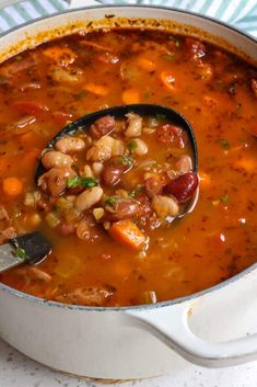 a spoon full of beans and carrots in a white pot with a blue striped napkin