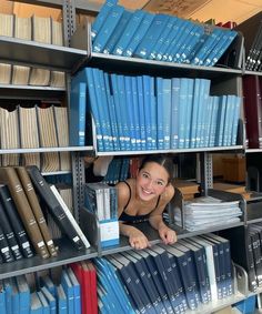 a woman is peeking out from behind a book shelf filled with books and binders